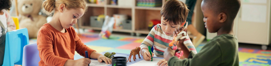 Children engaged in hands-on learning activities at a classroom table with art supplies and educational toys