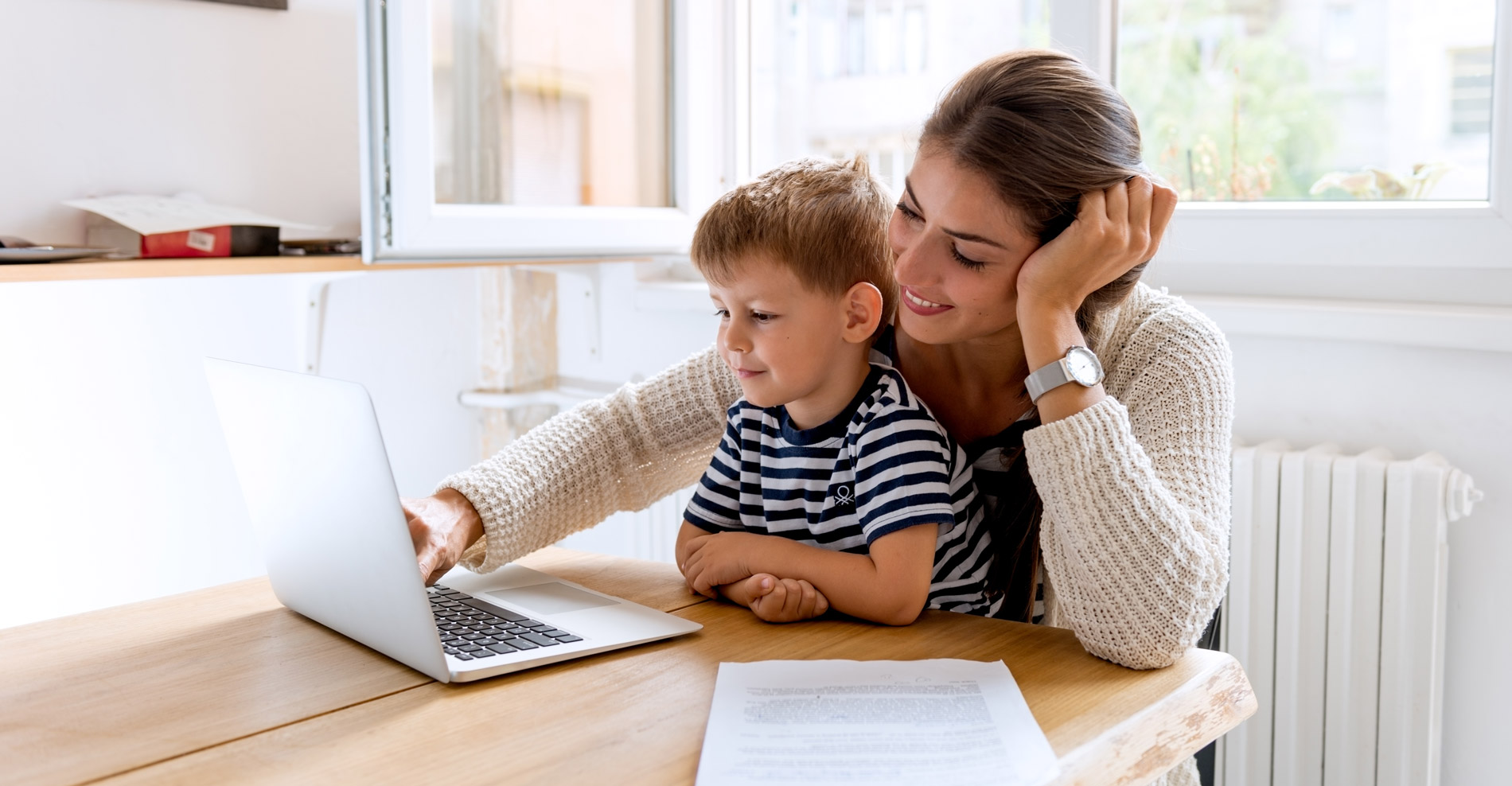 Mother and child sitting at a table looking at a laptop learning about daycare tuition and enrollment for preschool
