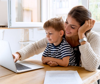 Mother and child sitting at a table looking at a laptop learning about daycare tuition and enrollment for preschool