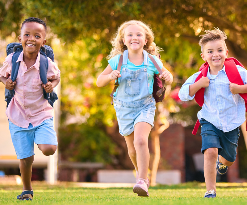 Group of Afterschool Care students running with excitement outside with their bookbags on their backs.