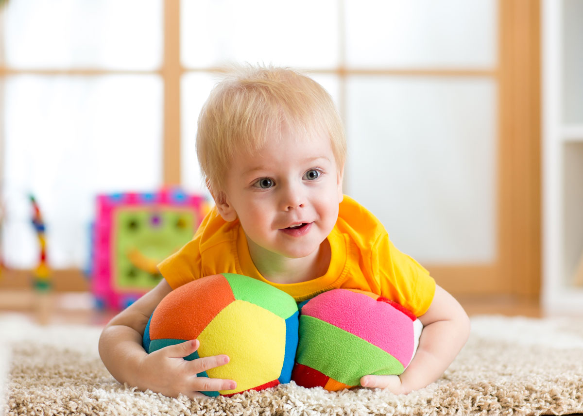 Early preschool child laying on carpet with two colorful stuffed toys in his arms