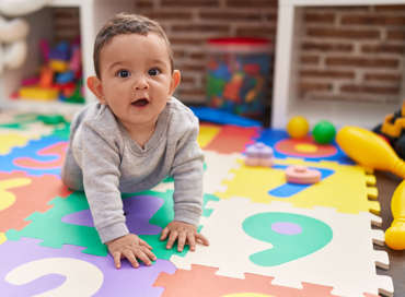 A curious baby boy crawling on a colorful number foam play mat surrounded by toys, representing the toddler program