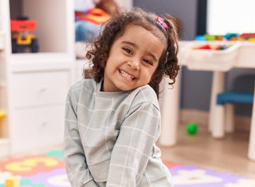 Smiling GA Pre-K student sitting in a daycare classroom with colorfule toys in the background.
