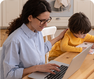A woman wearing glasses sitting with a child at a table while using a laptop together