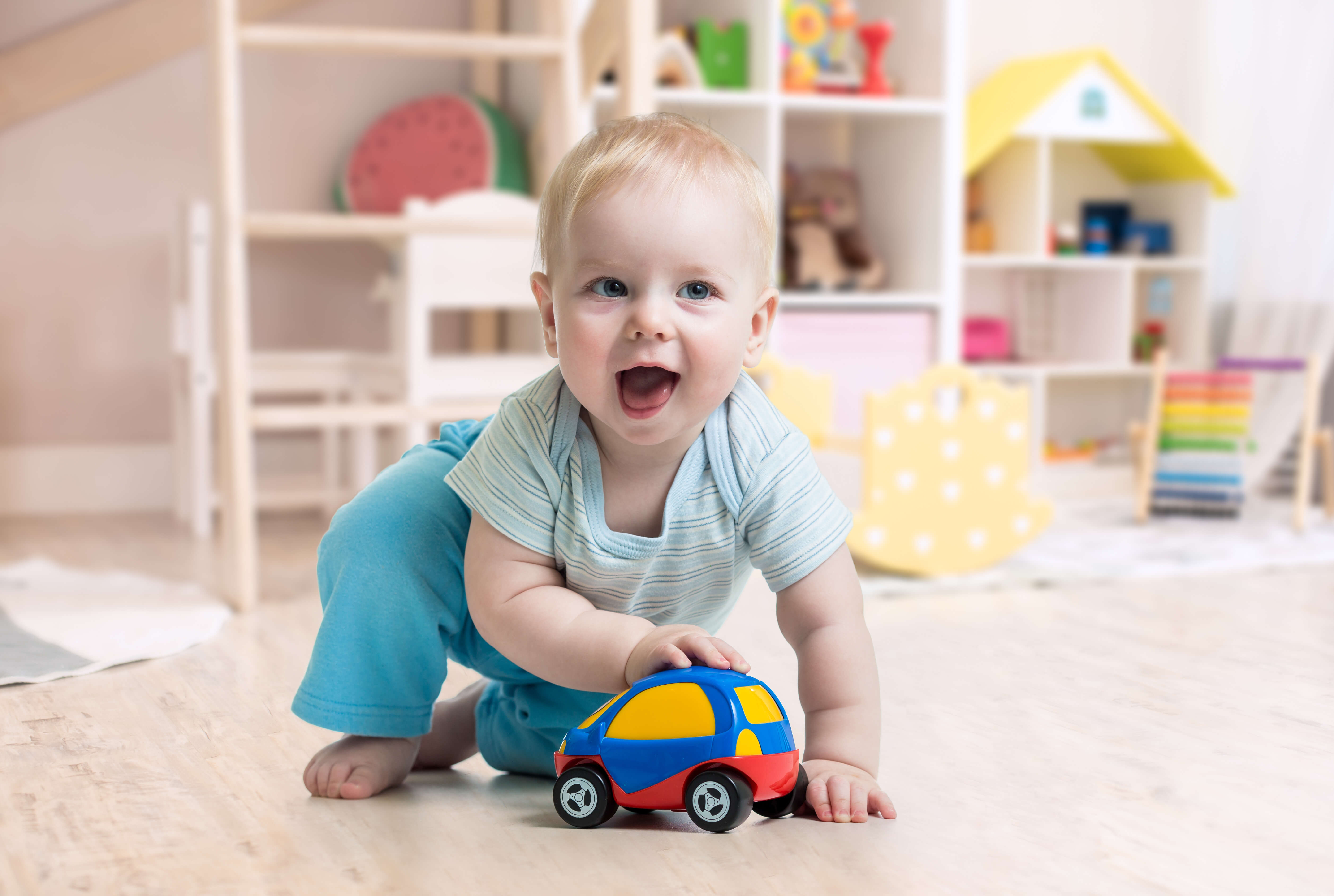 Smiling toddler crawling on the floor and playing with a colorful toy car