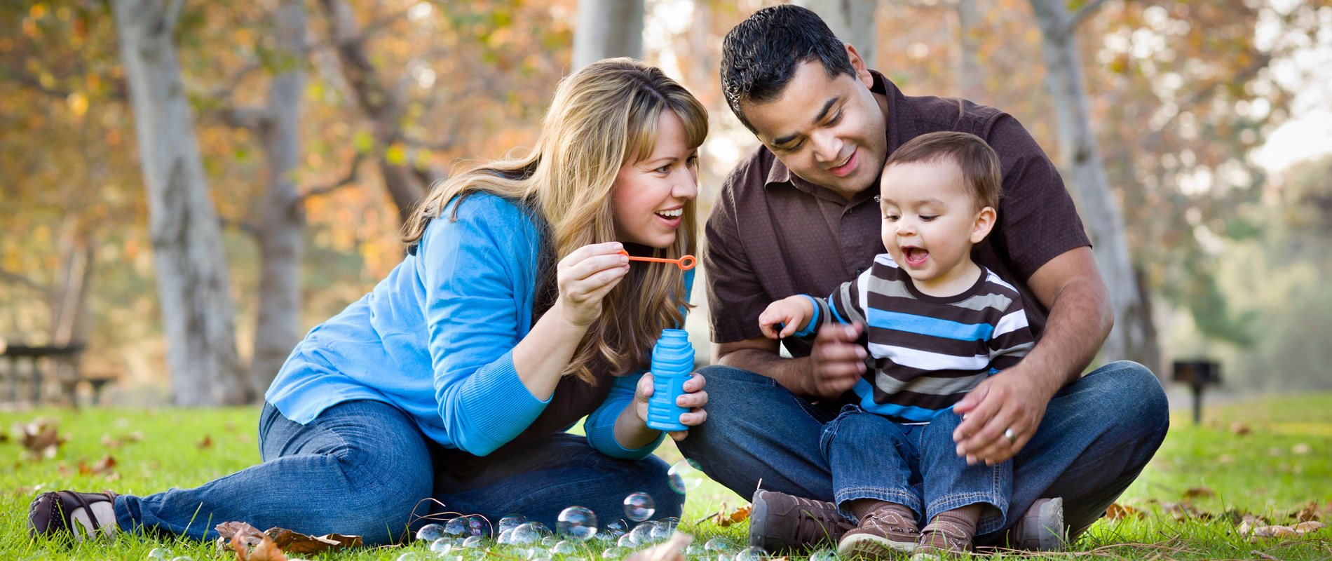 Family sitting outside blowing bubbles with their toddler child