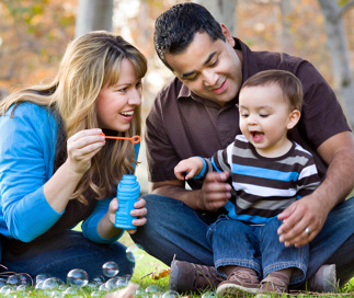 Family sitting outside blowing bubbles with their toddler child