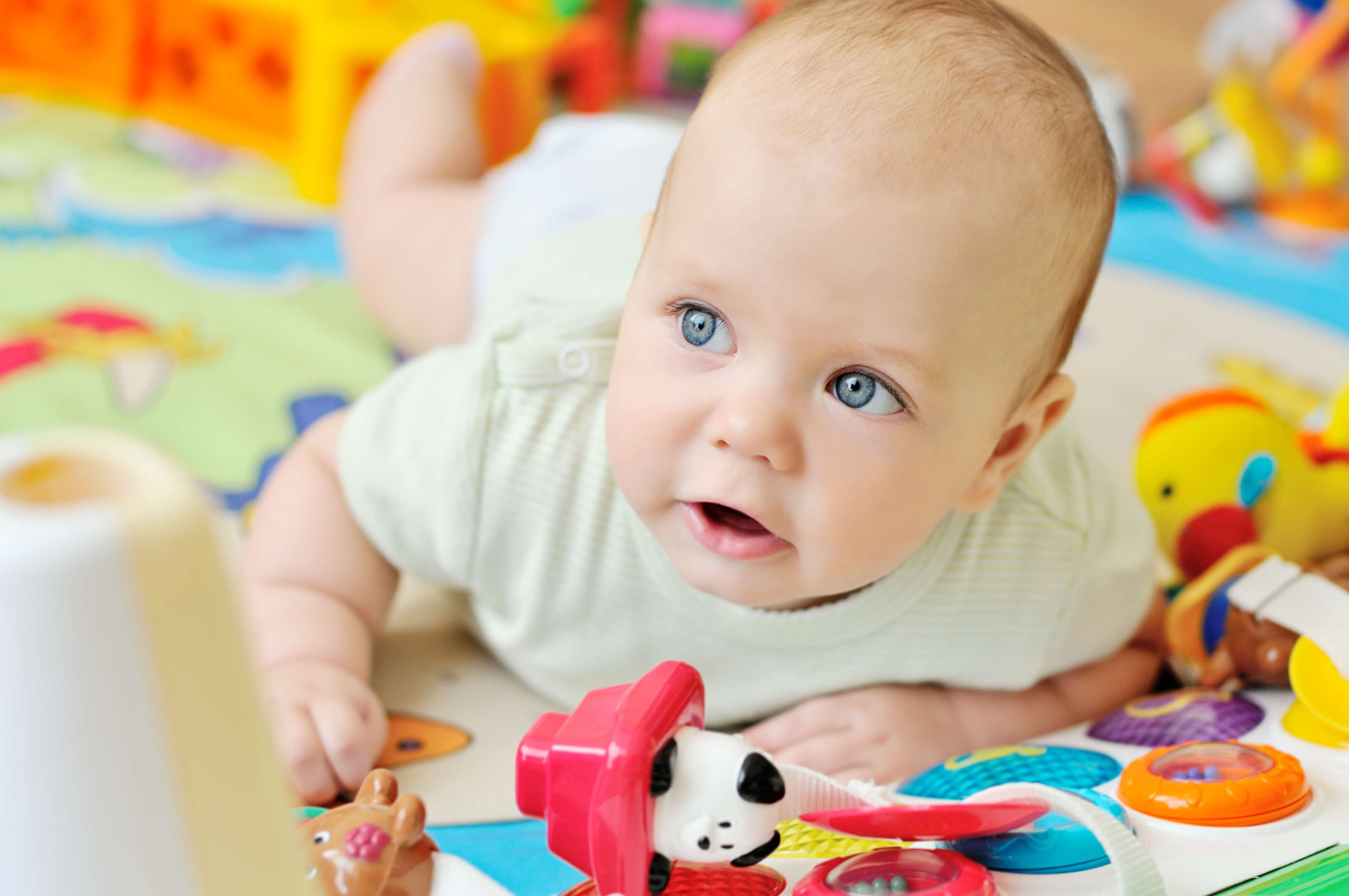 Baby doing tummy time on a colorful play mat surrounded by infant toys