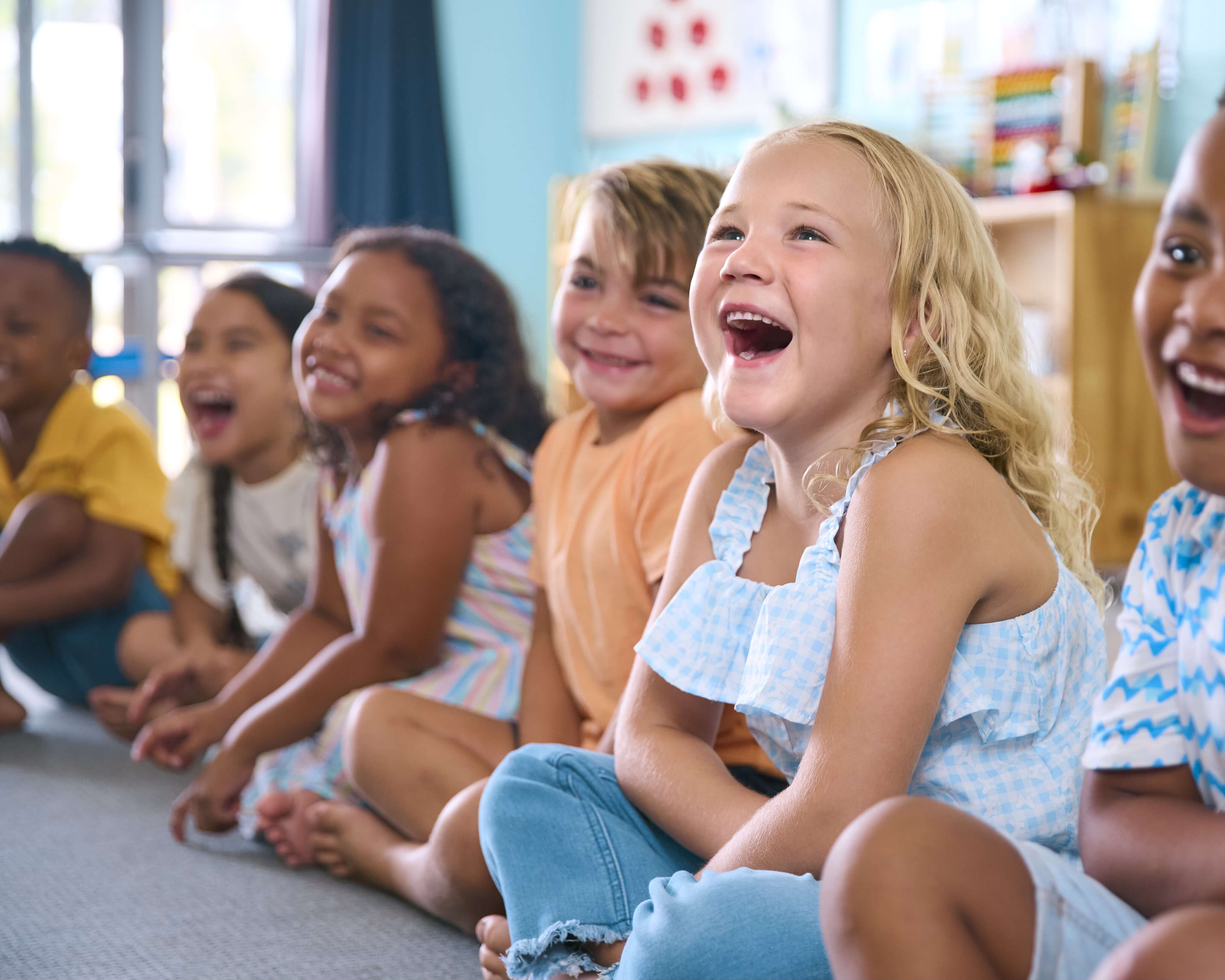 A group of diverse children sitting on the floor in a classroom, all laughing and smiling joyfully together
