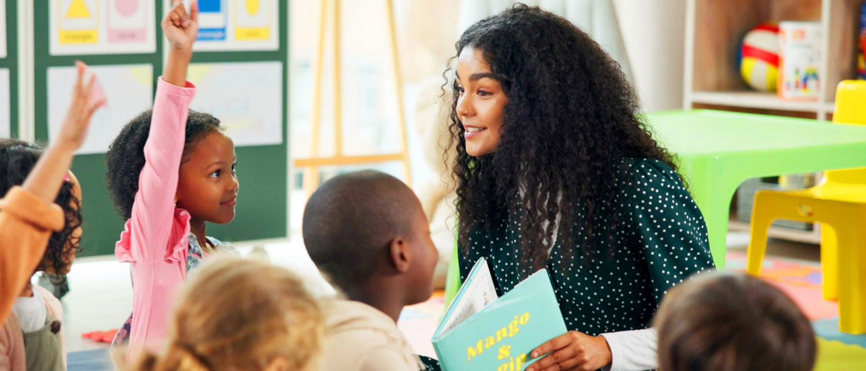 Young teacher reading to a group of engaged children in a classroom