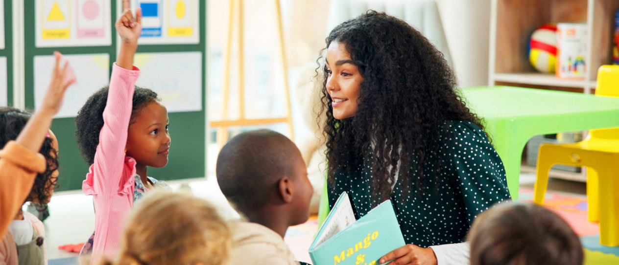 Young teacher reading to a group of engaged children in a classroom