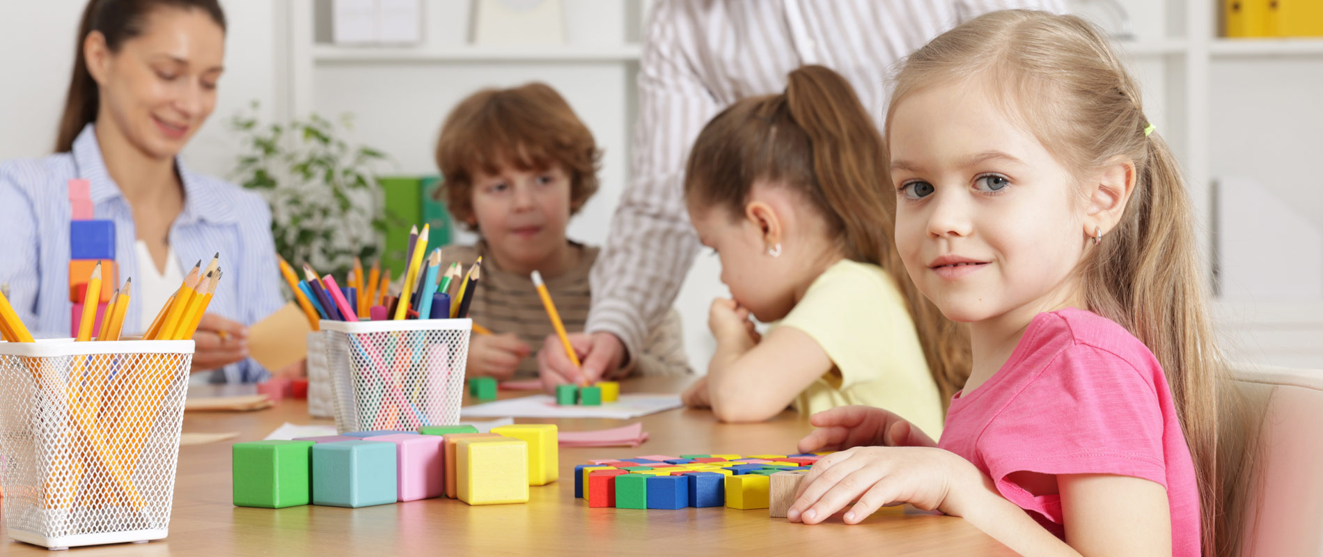 Children at table in daycare doing STEAM activities with coloring and blocks