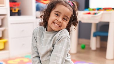 Pre-K girl smiling in a gray sweater in a daycare classroom