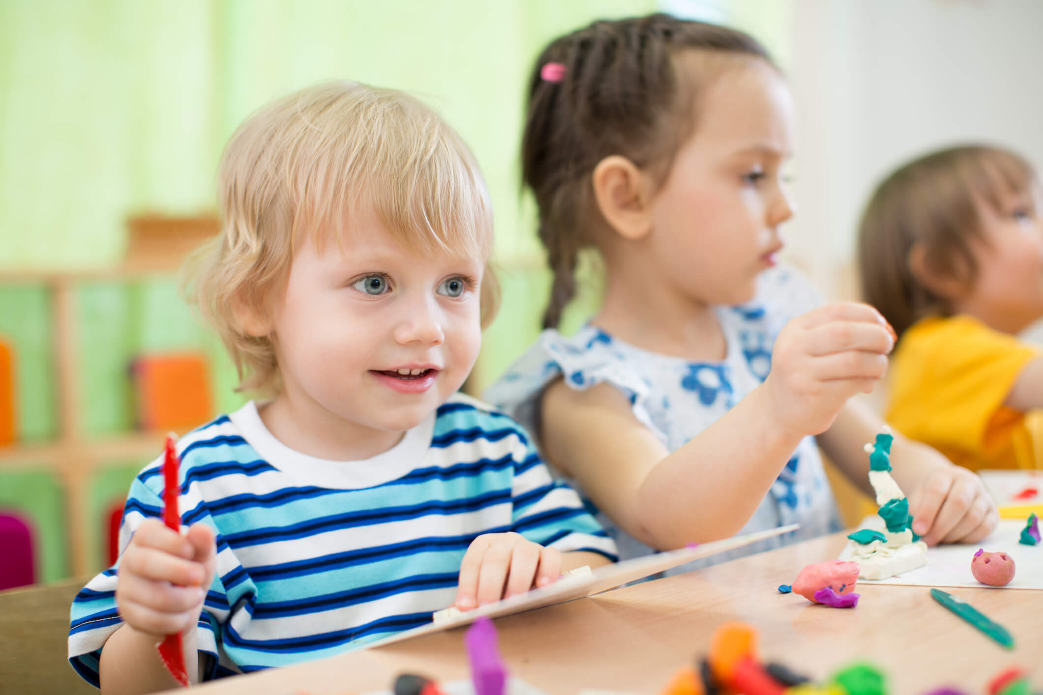 Young children working with clay and art supplies at a preschool classroom table