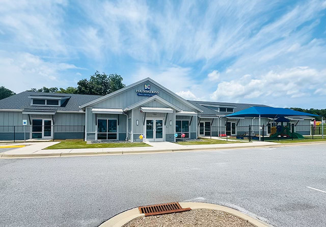 Exterior view of a Foundations Early Learning Center building with covered playground area on a sunny day