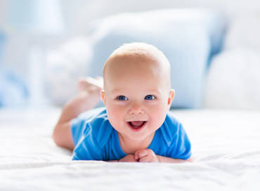 A smiling baby with blue eyes during tummy time in a soft bright environment, representing the infant care program