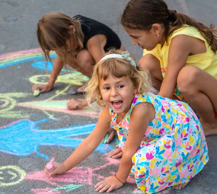 Pre-K children coloring pictures outside with sidewalk chalk.